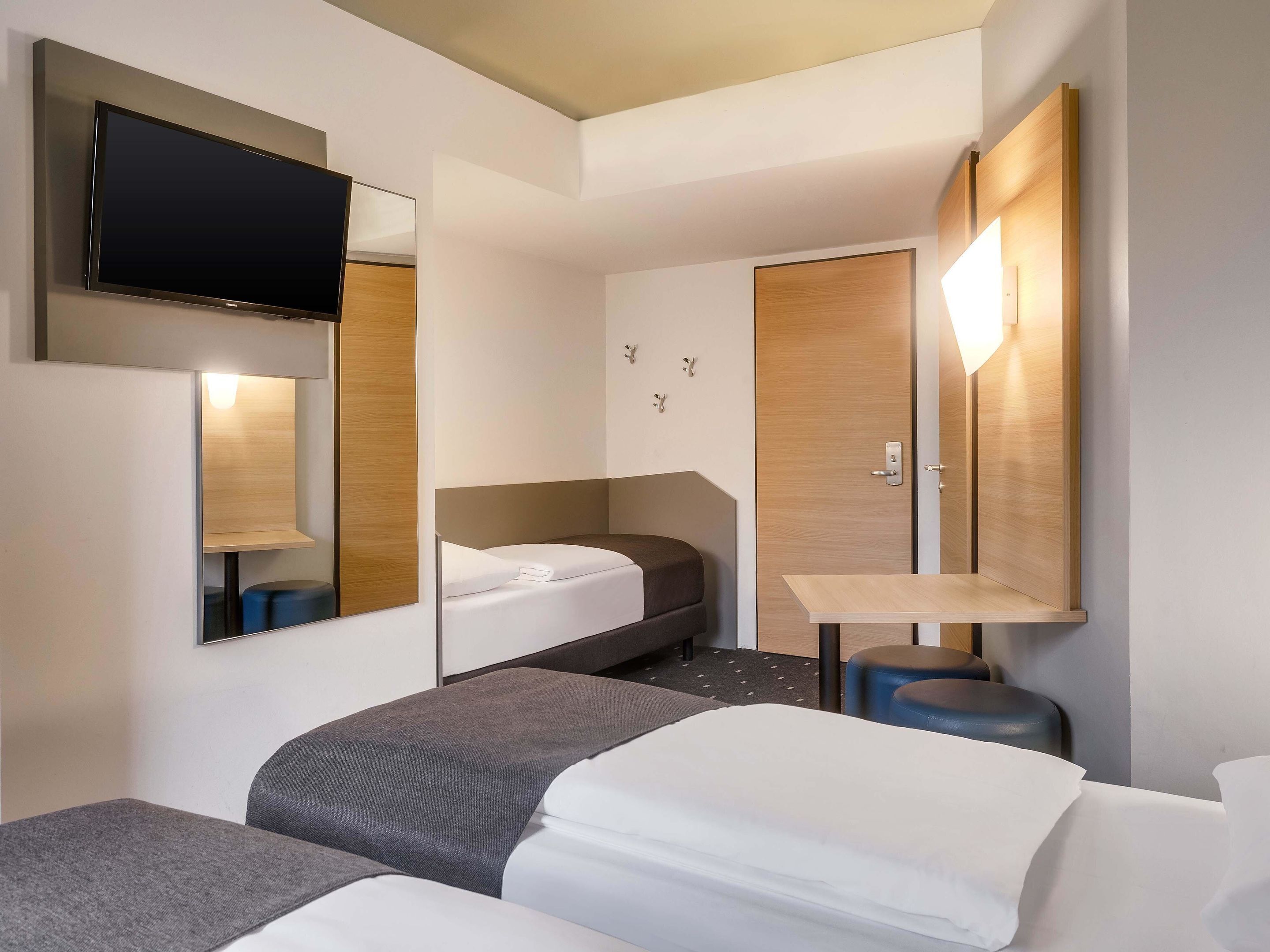 Une chambre d’hôtel moderne équipée d’un lit, d’un bureau, d’une chaise et d’un téléviseur fixé au mur.