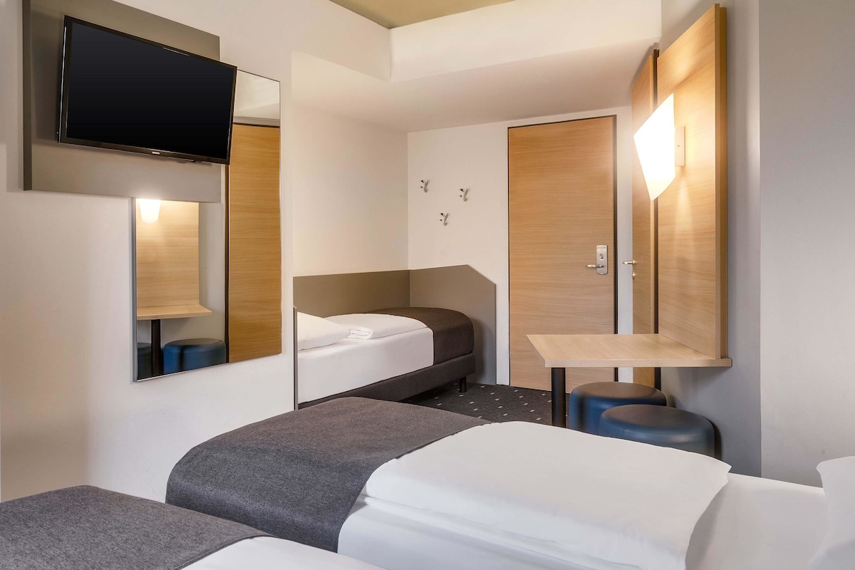 Una habitación de hotel moderna con una cama, un escritorio, una silla y un televisor fijado a la pared.