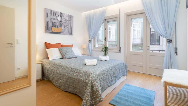 A bedroom with a bed, a nightstand, a window with curtains, a wall-mounted artwork, and a door. - Colorful Bright Flat w/ Balcony by HostWise (Porto)