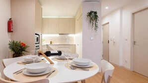 A dining area with a round table set for four, white chairs, and a kitchen in the background. - Colorful Bright Flat w/ Balcony by HostWise (Porto)