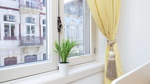 A window with a potted plant, a yellow curtain, and a view of buildings. - Colorful Bright Flat w/ Balcony by HostWise (Porto)