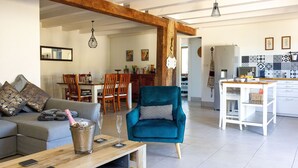 A spacious living area with a grey sofa, a teal armchair, and a wooden coffee table. A dining area with wooden chairs and a table is visible in the background. - Peaceful Countryside Gite with private pool near Aubeterre (Laprade)