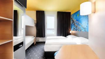 Une chambre d’hôtel avec des lits superposés, un bureau, une chaise, une fenêtre avec des rideaux et une lampe fixée au mur.