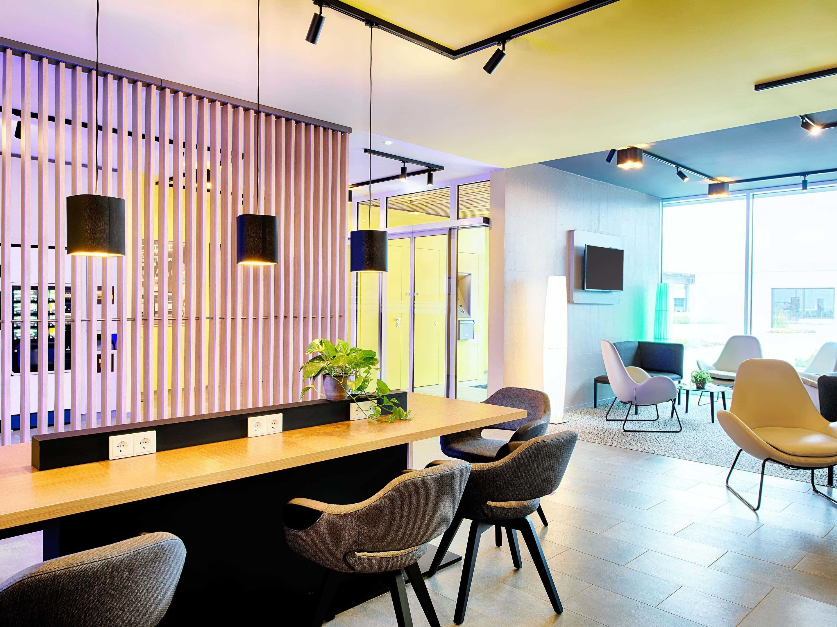 Un área de recepción moderna con un panel de listones de madera, un mostrador de recepción y varias zonas de estar con sillas.