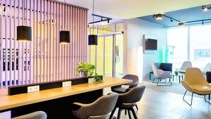 A modern reception area with a wooden slat partition, a reception desk, and several seating areas with chairs. - B&B Hotel Rust-Ettenheim (Mahlberg)