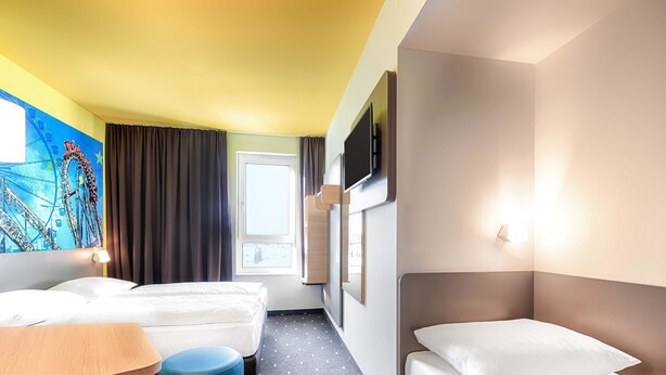 A hotel room with two beds, a desk, and a chair. - B&B Hotel Rust-Ettenheim (Mahlberg)