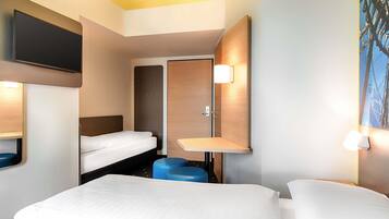 A hotel room with two beds, a flat-screen TV, a wooden headboard, a small seating area, and a painting on the wall.