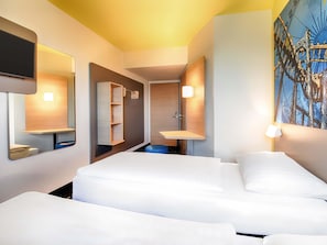 Ein Hotelzimmer mit zwei Betten, einem Badezimmer mit Waschbecken und Spiegel sowie einem Bild an der Wand.
