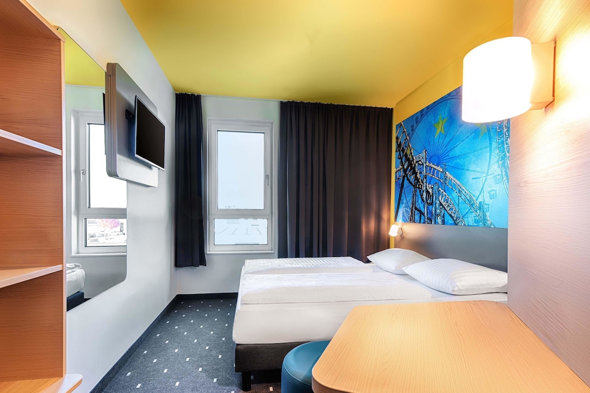 Ein Hotelzimmer mit Bett, Schreibtisch, Fernseher und Fenster.