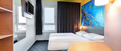 Ein Hotelzimmer mit Bett, Schreibtisch, Fernseher und Fenster.