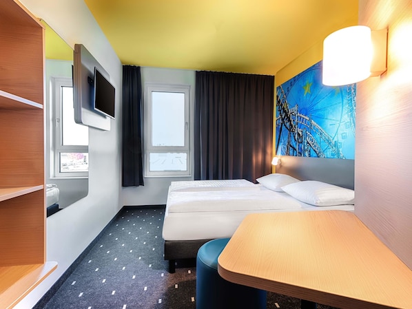 Ein Hotelzimmer mit Bett, Schreibtisch, Fernseher und Fenster.