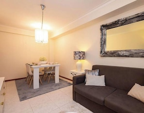 A modern living room with a dining area, a large mirror, and a chandelier.