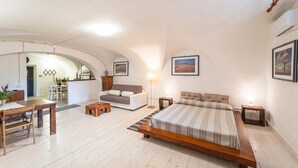 A spacious bedroom with a large bed, a dining area, and a kitchen in the background. - Loft Apartment ‘Casa Gilbert 101’ close to Beach with Wi-Fi (alghero)
