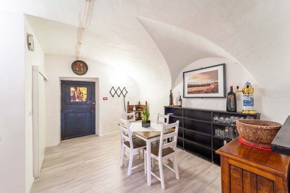 Zona pranzo con tavolo e sedie, camino, mensola con bicchieri e un quadro incorniciato al muro.
