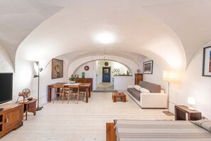 An arched ceiling, a dining area with chairs and a table, a sofa, a bed, and a lamp.