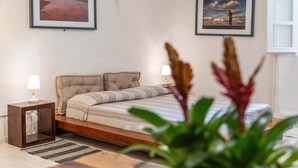 A bedroom with a bed, two bedside lamps, a framed landscape painting, a window, and a potted plant. - Loft Apartment ‘Casa Gilbert 101’ close to Beach with Wi-Fi (alghero)