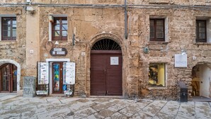 A stone building with a large arched entrance, a shop with a signboard, and a small display window. - Loft Apartment ‘Casa Gilbert 101’ close to Beach with Wi-Fi (alghero)