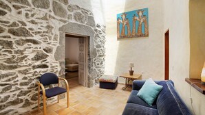 Una habitación con pared de piedra, puerta de madera, sofá azul y una pequeña mesa con lámpara.