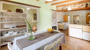 Un comedor con una mesa dispuesta para dos personas, una cocina al fondo y una estantería con cristalería.