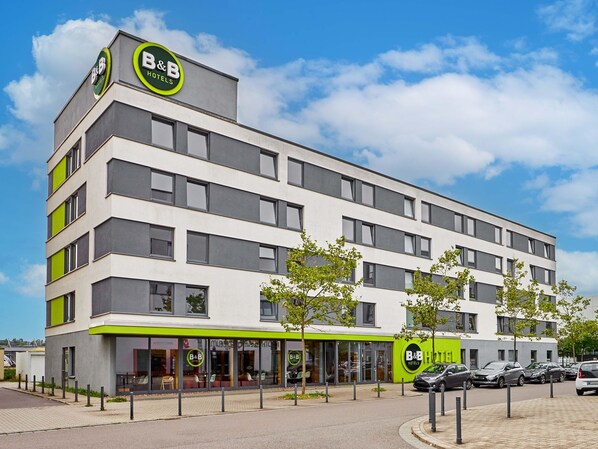 Un hôtel-boutique moderne, caractérisé par une façade sobre, de grandes fenêtres et une touche de vert sur le niveau inférieur.