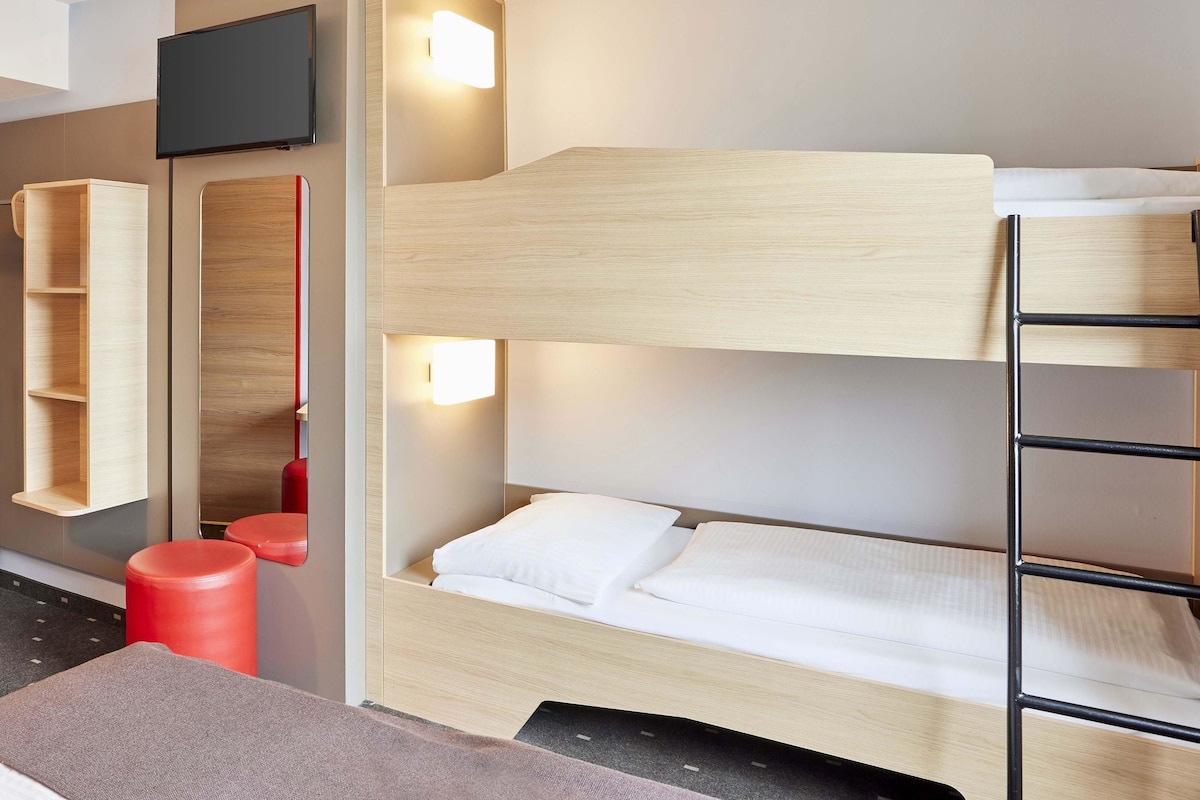 A bunk bed room with a television, a shelf, and a red stool.