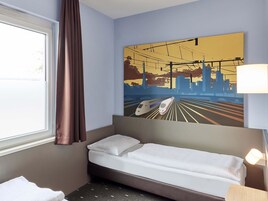 Una habitación de hotel con una cama, una ventana con cortinas, un cuadro colgado en la pared de un tren y una lámpara de noche.