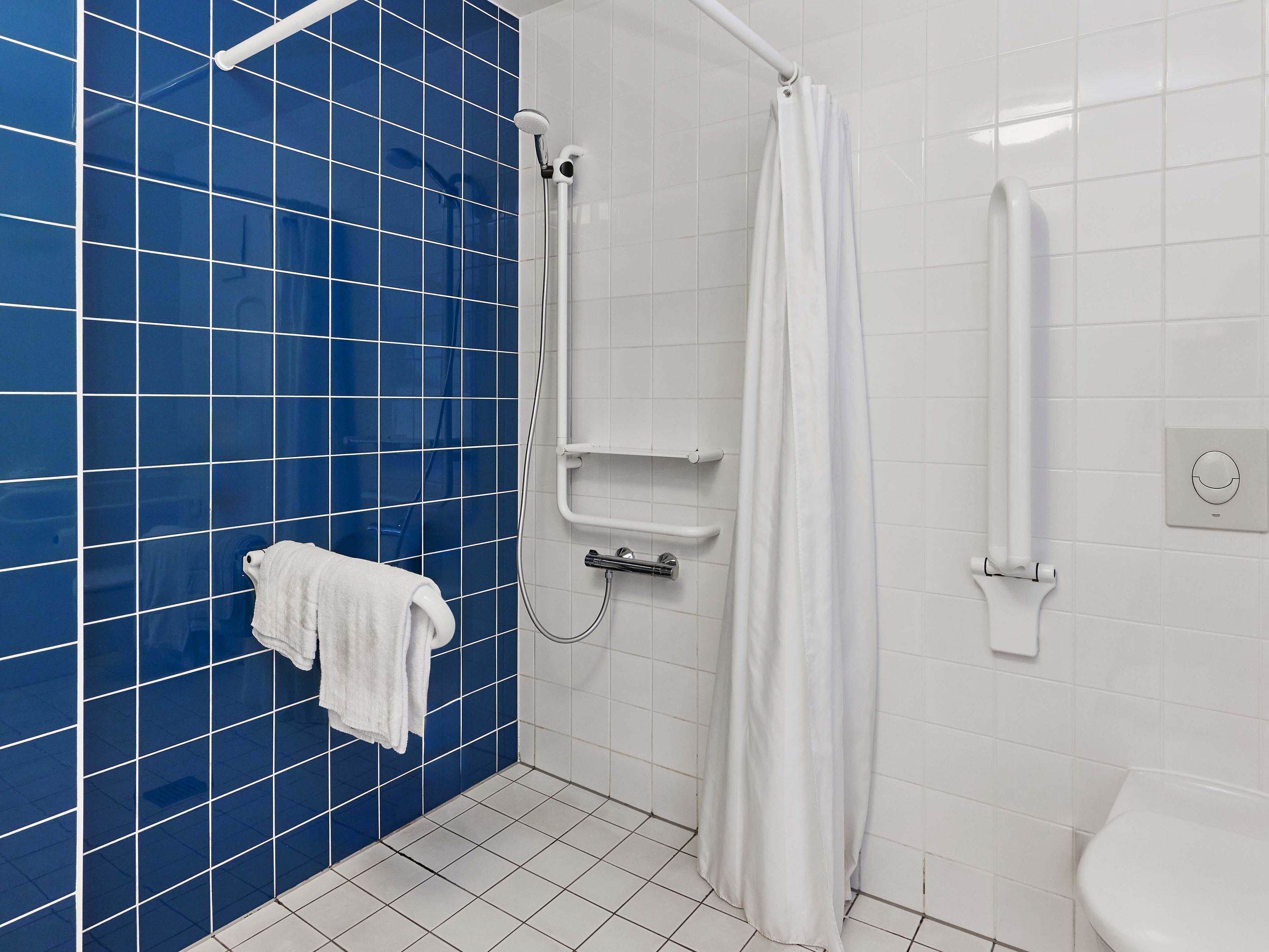 A bathroom with blue tiled walls, a white toilet, a shower area with a white curtain, and a towel rack with a white towel.