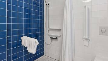 A bathroom with blue tiled walls, a white toilet, a shower area with a white curtain, and a towel rack with a white towel.