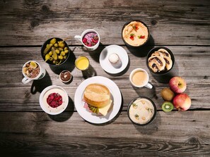 A variety of breakfast items including pancakes, a sandwich, and fresh fruits like apples and kiwi on a wooden table.