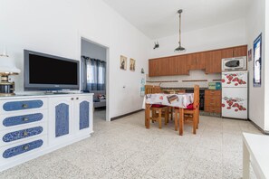 A compact kitchen with a TV, wooden cabinets, a microwave, and a dining area with a table and chairs. - Holiday Home "El Graciosero" close to the Beach with Sea View, Wi-Fi & Terrace (Caleta de Sebo)