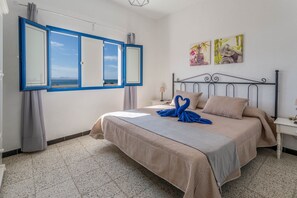 A bedroom with a bed, a nightstand, a window with curtains, and wall art. - Holiday Home "El Graciosero" close to the Beach with Sea View, Wi-Fi & Terrace (Caleta de Sebo)
