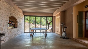 A spacious indoor area with a concrete floor, a table with chairs, a treadmill, and a fan. - Beautiful Holiday Home “Son Llodra” with Mountain View, Pool, Terrace & WiFi (Son Macia)