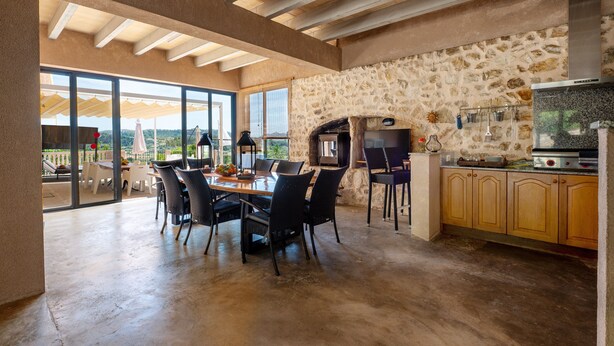 A spacious kitchen with a stone wall, a built-in oven, and a large dining table with chairs. - Beautiful Holiday Home “Son Llodra” with Mountain View, Pool, Terrace & WiFi (Son Macia)