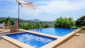 A rectangular swimming pool with a clear blue water feature, surrounded by a beige tiled deck, a white umbrella, and a stone planter. - Beautiful Holiday Home “Son Llodra” with Mountain View, Pool, Terrace & WiFi (Son Macia)