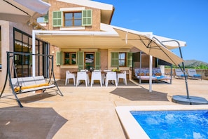 A poolside area with a covered seating area, a table, and a swing chair.