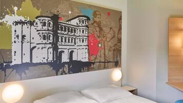 Habitación de hotel con cama, mesita de noche, lámpara de pared y un cuadro abstracto de gran tamaño.
