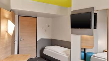 Una habitación de hotel con cama, escritorio, silla, televisor y espejo.