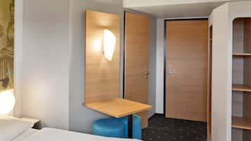 A hotel room with a bed, a desk, a wardrobe, and a blue chair.