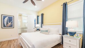 Une chambre à coucher avec un lit, des tables de chevet, un ventilateur de plafond et une fenêtre avec des rideaux.