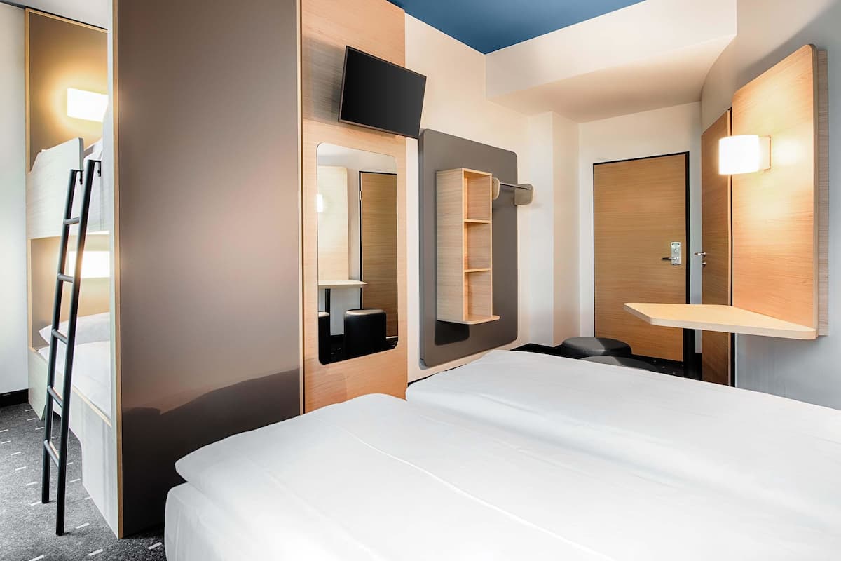 Quarto de hotel moderno com uma cama grande, televisão presa na parede, um espelho e uma estante de madeira.