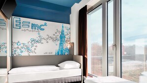 A modern hotel room with a large window, a bed, a desk, and a wall with a scientific-themed mural. - B&B Hotel Ulm (Ulm)