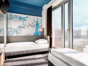 Quarto de hotel moderno com uma janela ampla, uma cama, uma escrivaninha e uma parede com um mural de tema científico.