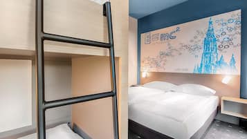 A hotel room with a bunk bed, a large bed, a wall with a cityscape artwork, and a nightstand.