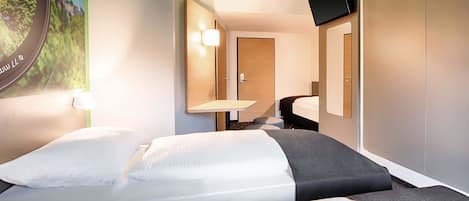 Ein Hotelzimmer mit zwei Betten, einem Schreibtisch, einem Stuhl, einem Fernseher und einem wandmontierten Spiegel.