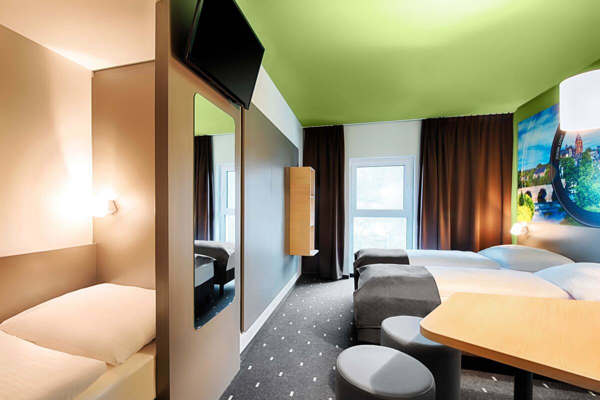 A hotel room with a bed, a desk, a chair, a TV, and a window with curtains.