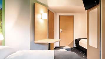 A hotel room with a bed, a bedside table, a TV mounted on the wall, and a door.
