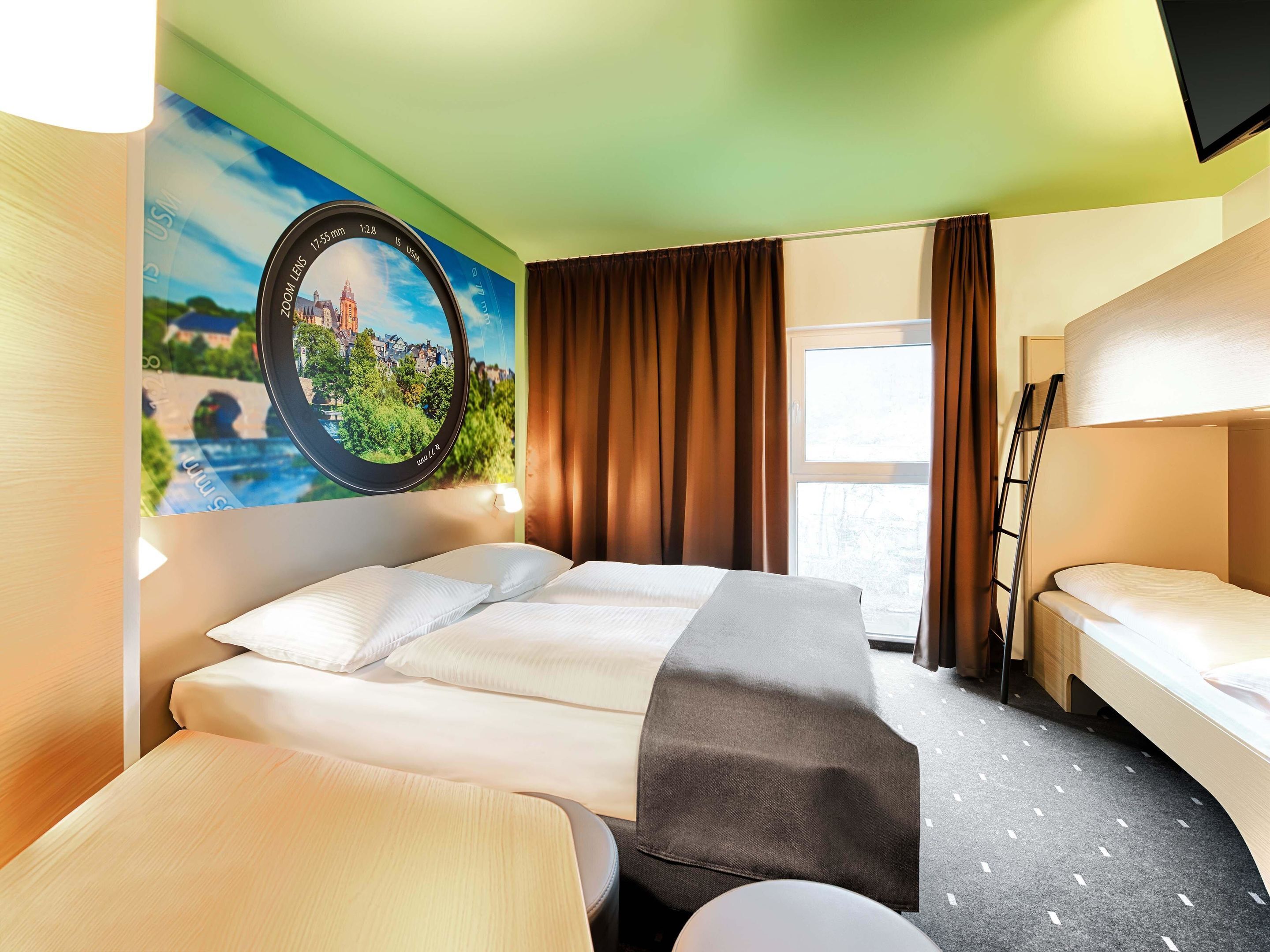 Habitación de hotel con cama, escritorio, silla, ventana con cortinas, un cuadro en la pared y una litera.