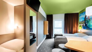 A hotel room with a bed, a desk, a chair, a TV, and a window with curtains.