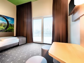 Una habitación de hotel moderna con una cama, un escritorio, una silla, un ventanal con cortinas y vistas a un paisaje nevado.