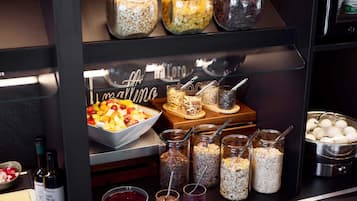 A buffet area with various food items, including a bowl of fruit salad, jars of nuts and seeds, and a bowl of red fruit compote.